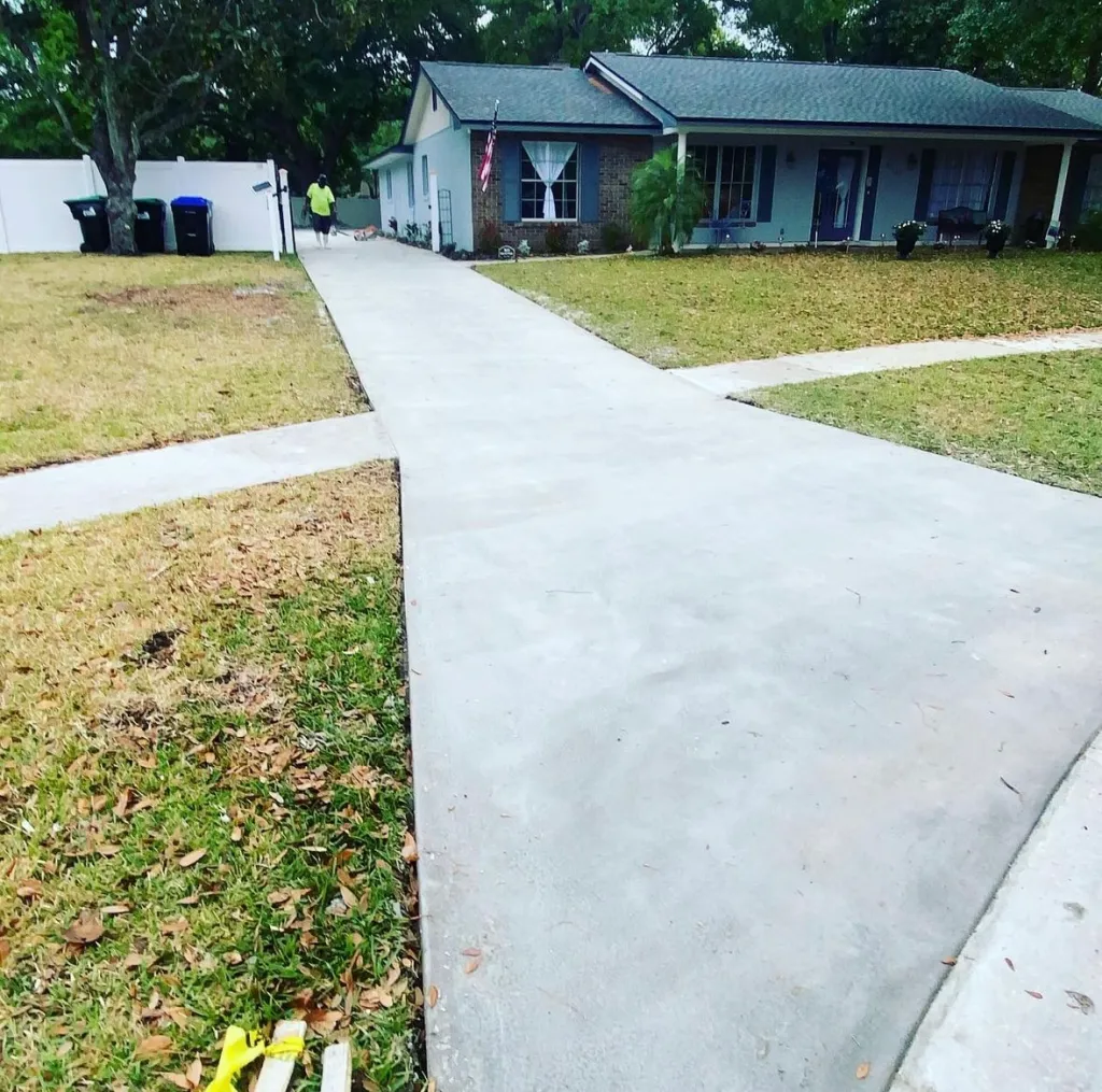 Freshly poured concrete driveway and walkway leading to a residential home in Central Florida, showcasing smooth surfaces and well-defined edges, with a person in a bright shirt walking nearby.