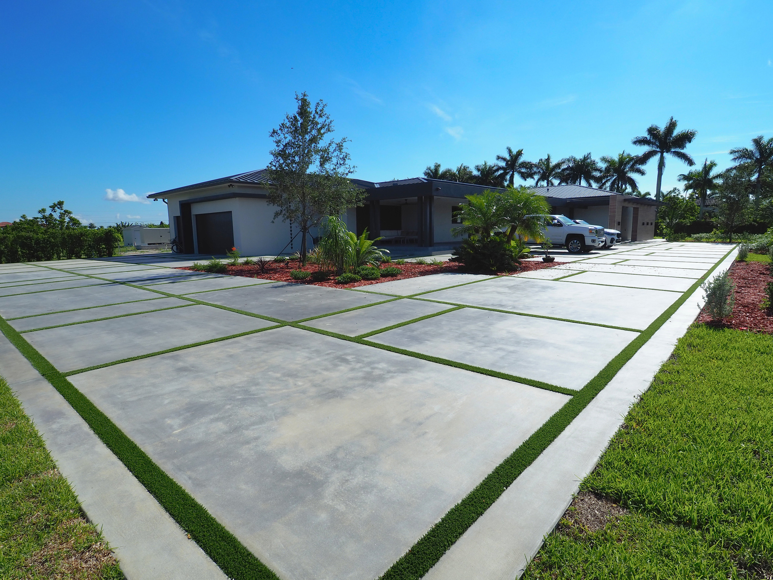 Modern concrete driveway with green grass accents, showcasing quality craftsmanship by Accu-Krete, Inc. in a residential setting, under a clear blue sky.