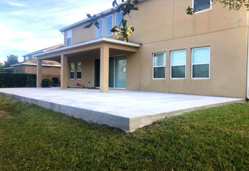Concrete patio slab in residential backyard, adjacent to house with beige exterior and large windows, showcasing Accu-Krete's quality concrete work for outdoor spaces.