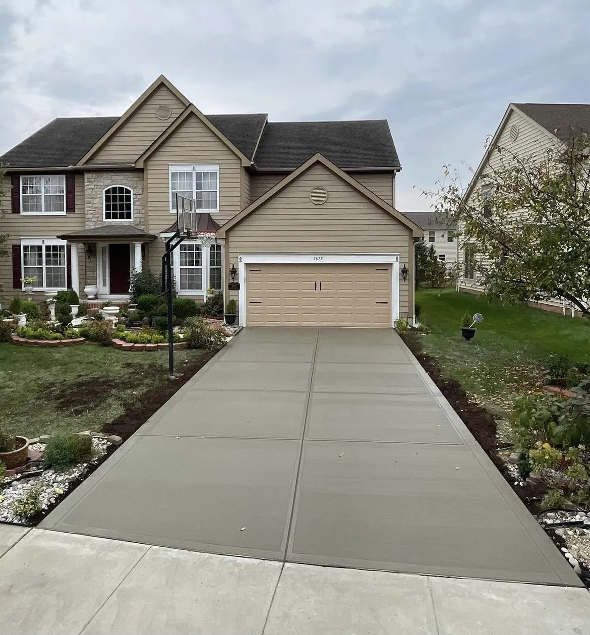 Newly poured concrete driveway in front of a residential home with landscaped garden and decorative features, showcasing Accu-Krete's quality concrete services.